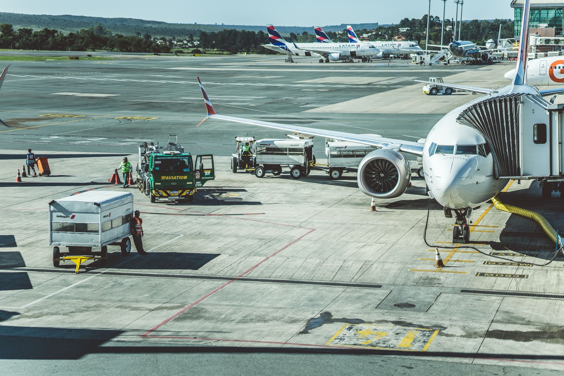 Ground crew and ground support equipment servicing an aircraft on the ramp, with other aircraft at the gate in the background.